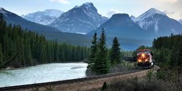 Train traveling through a scenic mountain landscape beside a river.