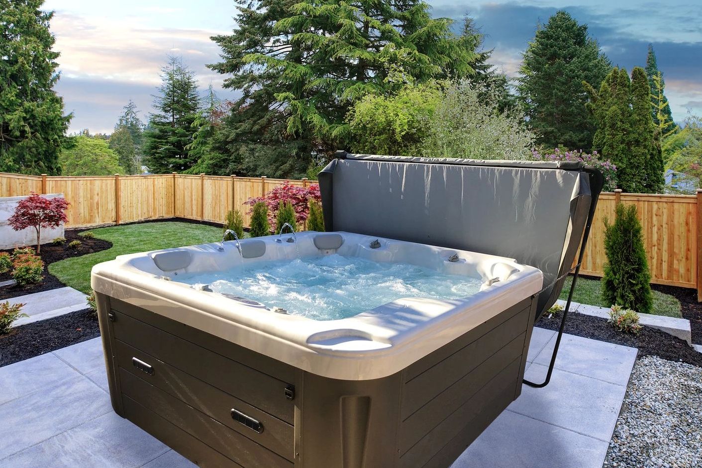Outdoor hot tub bubbling in a backyard surrounded by trees and a wooden fence.