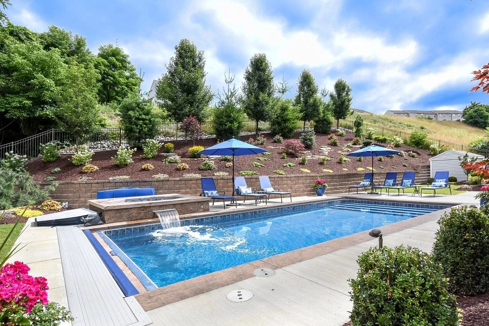 A serene backyard with a rectangular pool and blue lounge chairs under umbrellas.