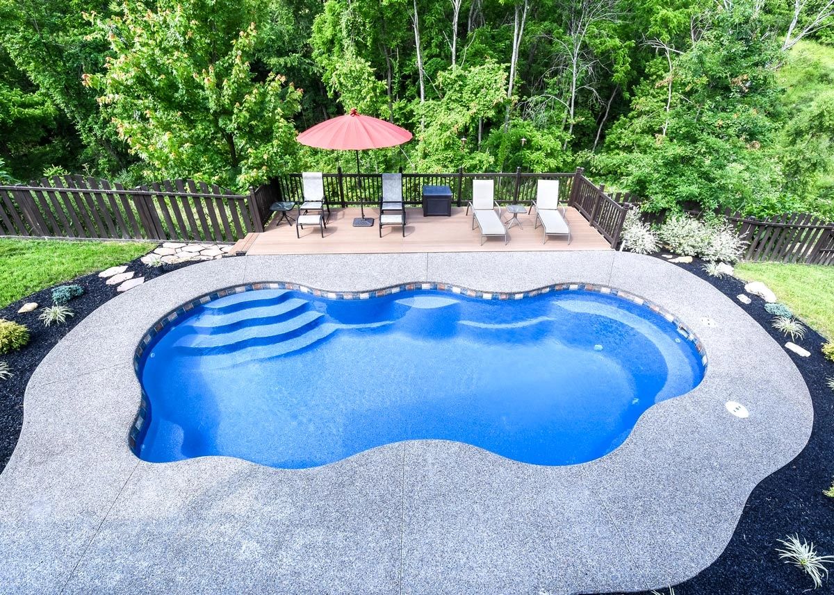Outdoor pool with deck chairs and green trees in the background.