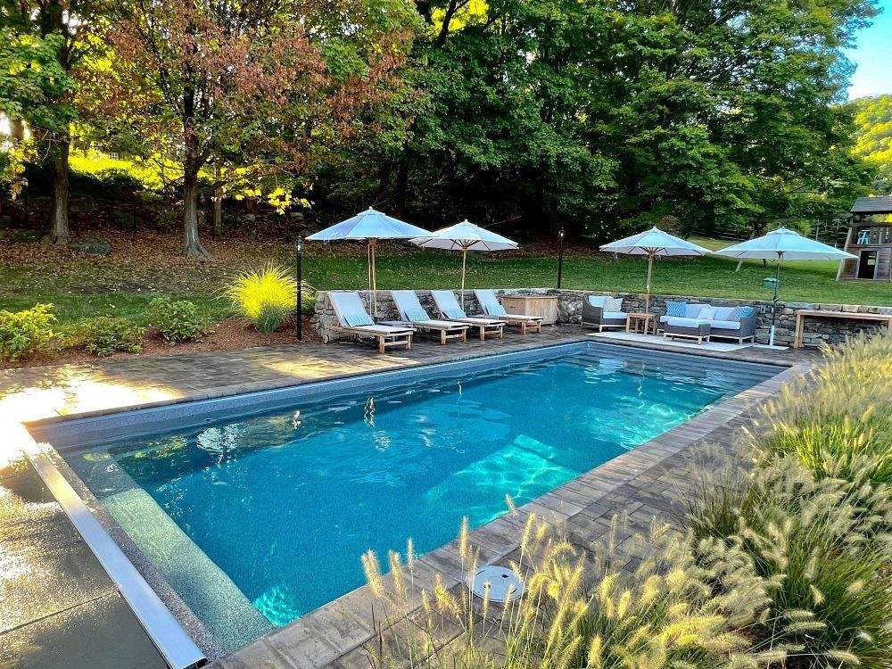 A serene backyard pool with lounge chairs and umbrellas surrounded by lush greenery.