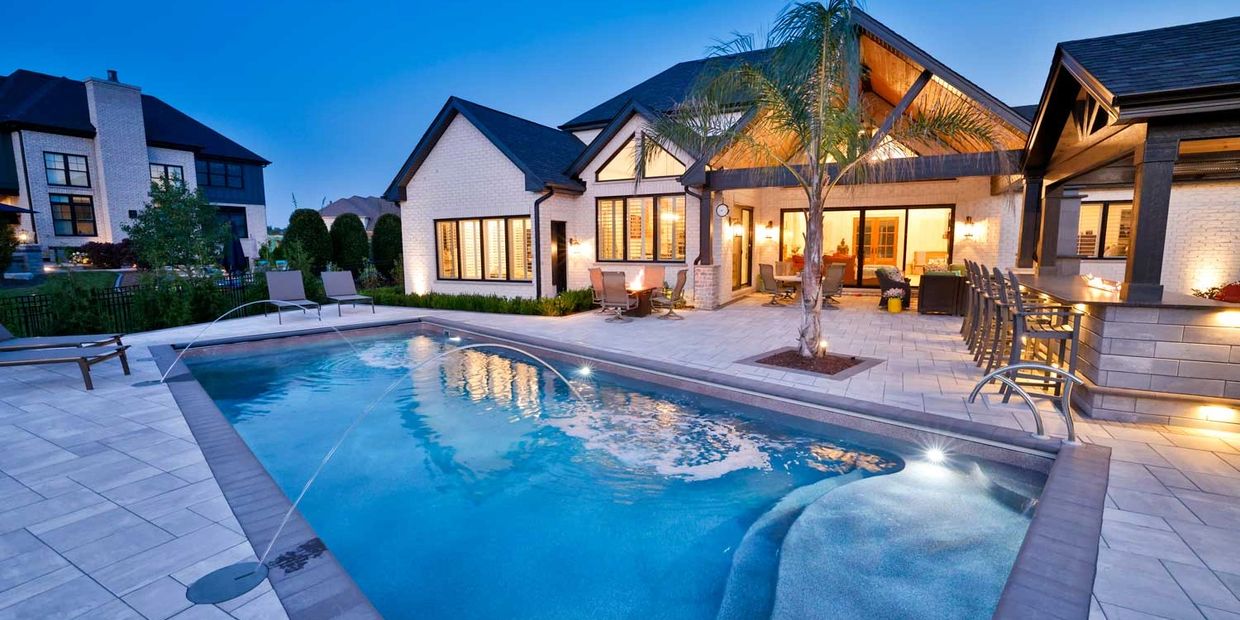 Modern house with a lit swimming pool and outdoor seating at dusk.