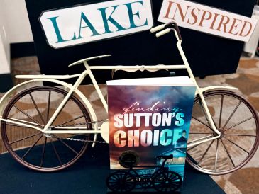 Decorative bicycle with 'Lake Inspired' signs and a book titled 'Finding Sutton's Choice'.