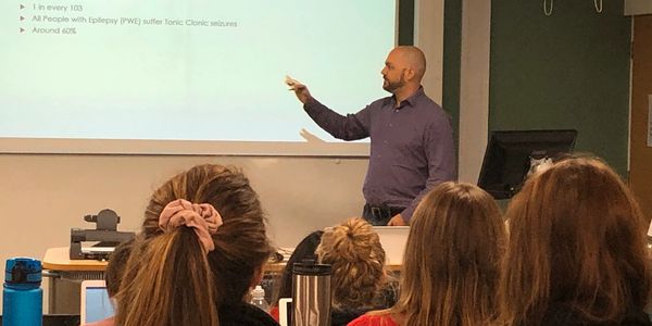 Simon gestures at a projected presentation whilst speaking to final year pharmacy students.