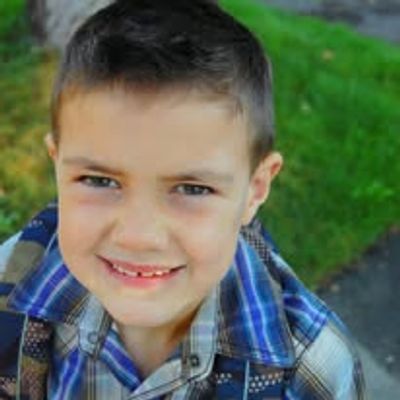 A smiling boy outdoors wearing a plaid shirt.