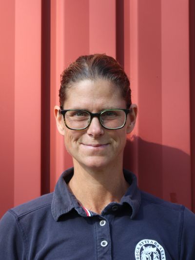 Woman with glasses smiling against a red wall background.