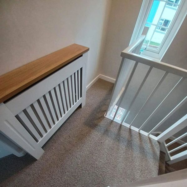 Carpeted stair landing with white railing and radiator cover.