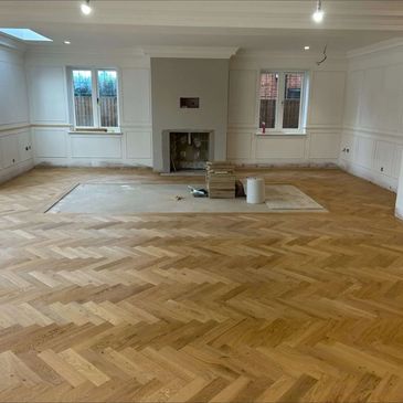 Spacious room with new herringbone wood flooring and white walls under renovation.