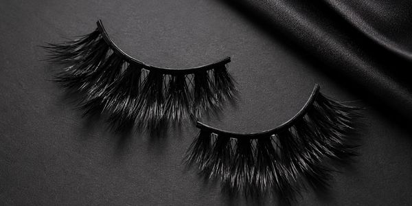 A pair of thick, black false eyelashes on a dark surface.