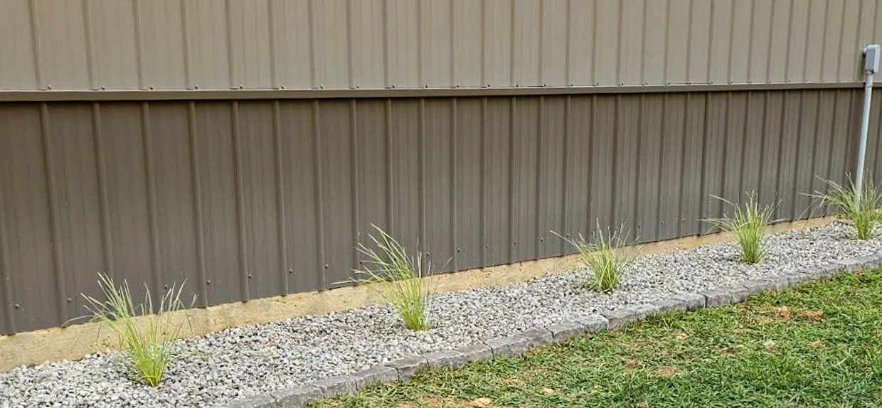 Simple landscaping with grass, gravel, and plants by metal wall.