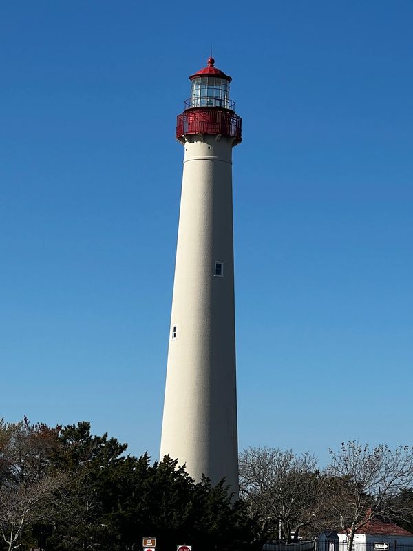 Tall white lighthouse with red top against clear blue sky.