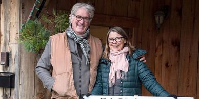 Un homme et une femme souriants devant une maison en bois.