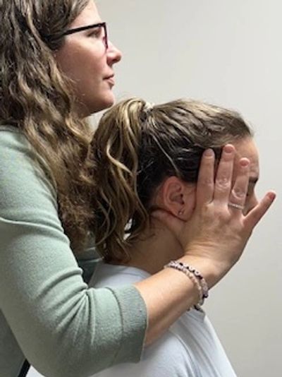 Female Chiropractor providing gentle neck and jaw screening while patient sits on treatment table. 
