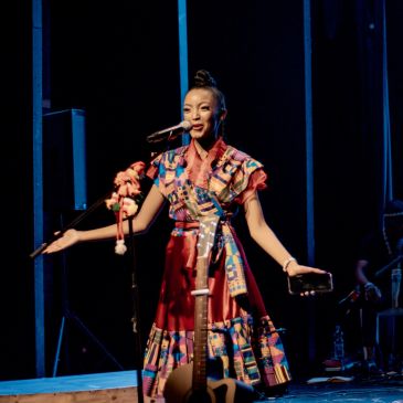 Woman speaking on stage with microphone, wearing colorful dress.