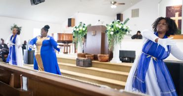 Women in blue and white dresses performing in a church.