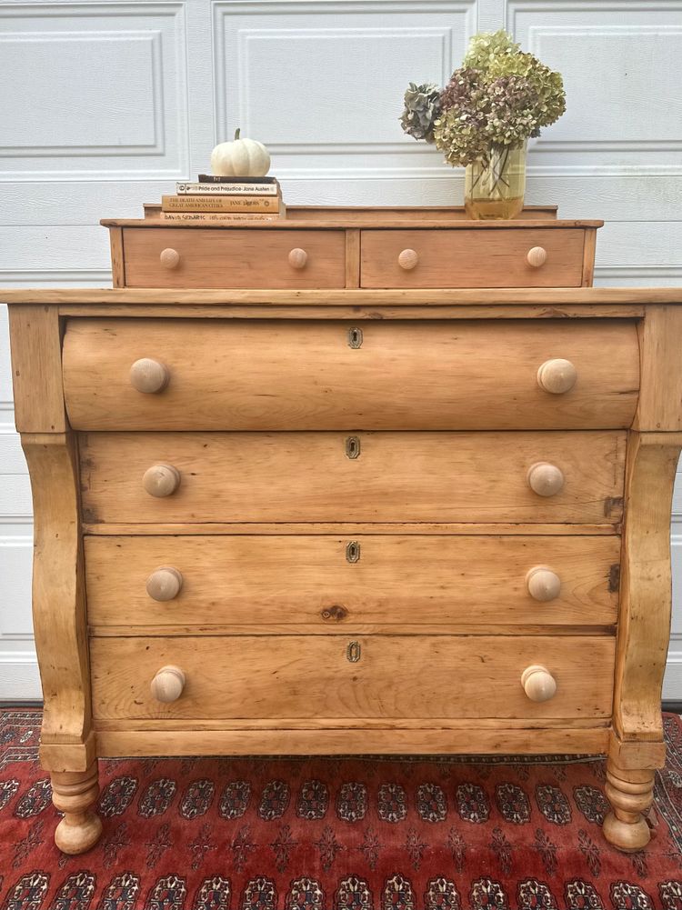 Antique wooden dresser with books, white pumpkin, and dried flowers on top.