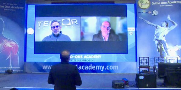 Picture of a man looking at screen of a video presentation with two men on the screen