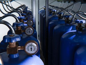 Rows of blue gas cylinders with pressure gauges connected by tubes.