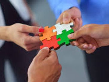 Four hands holding connected puzzle pieces of different colors.