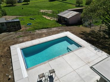 A small backyard pool with two chairs on a concrete patio.