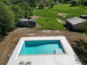 A rectangular backyard pool with clear water and a grassy field beyond.