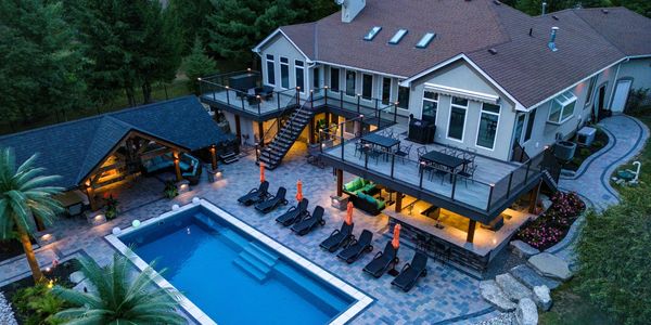 A luxurious house with tropically themed backyard including a large pool and outdoor lounge area.