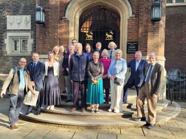 Group of well-dressed people posing outside a historic building on sunny day.