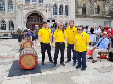 Four people in yellow shirts posing near barrels outdoors.