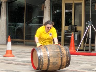 Person in yellow shirt rolling a wooden barrel outdoors.