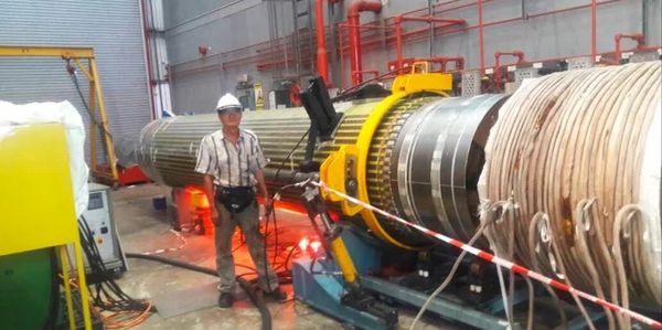 Technician in safety gear inspects large industrial turbine inside factory.