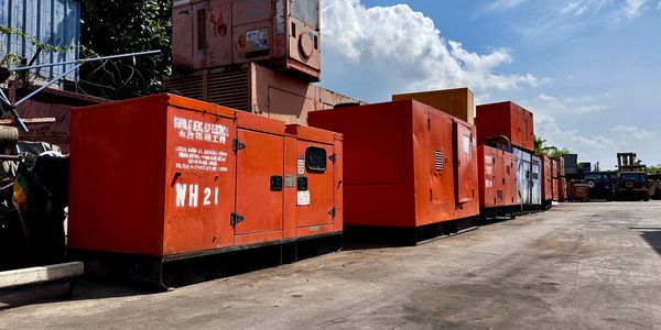 Row of large red industrial generators lined up outdoors under a sunny sky.