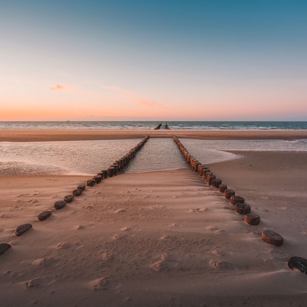 Wooden groynes leading into the calm sea during a pastel sunset.