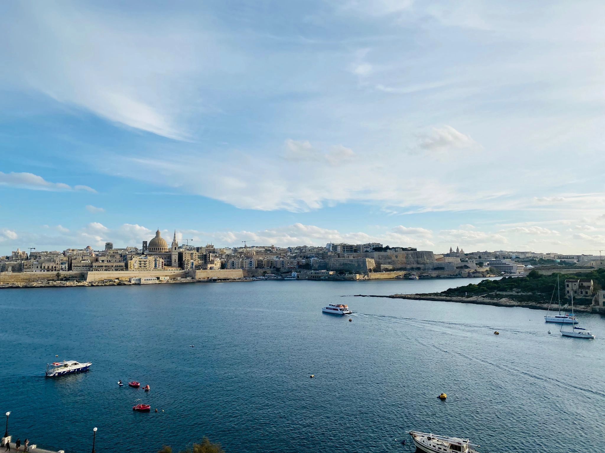 Scenic view of a historic city by the sea with boats on calm waters under a blue sky.