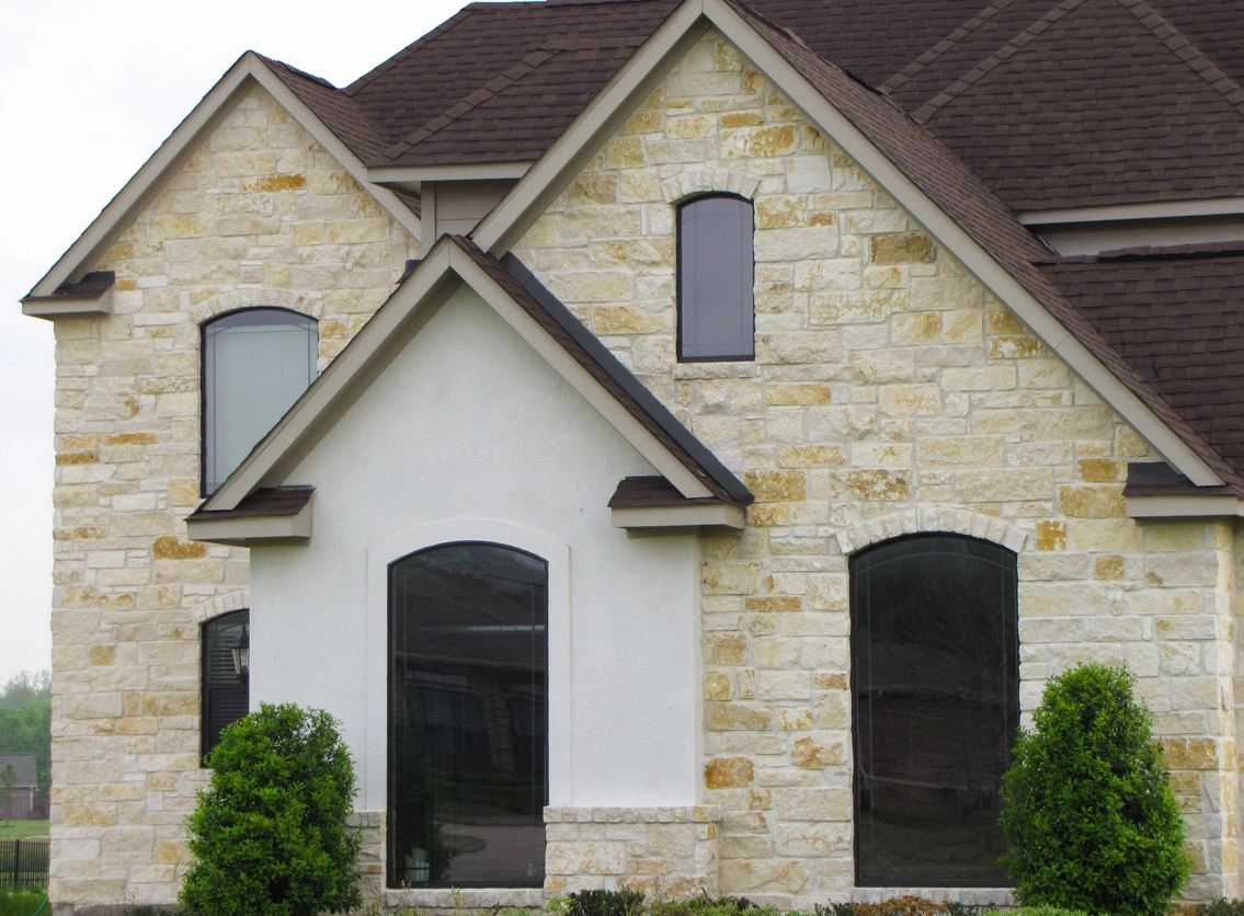 A house with a cream-yellow stone facade and a small section with white stucco