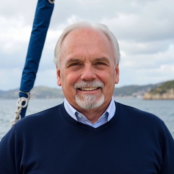 Smiling older man on a boat with water and hills in the background.