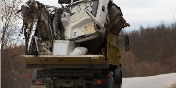 A truck carrying a large, crushed vehicle frame on a road.