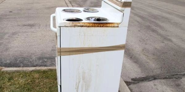 Old, rusty stove left outdoors, taped shut.