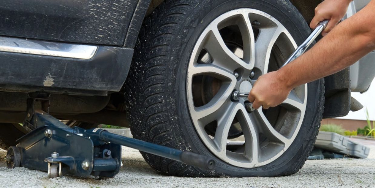 Person using a wrench to fix a flat tire on a car.