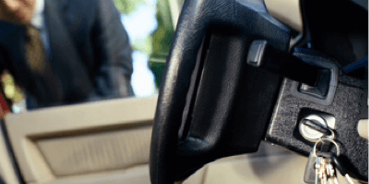 Car keys left in ignition with blurred man outside car door.