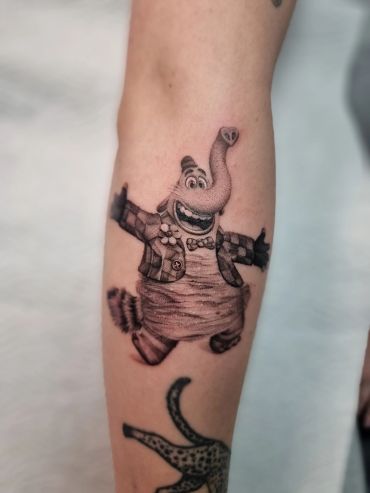 Tattoo of a joyful cartoon elephant character on forearm.
