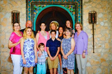 A multigenerational family poses in front of a decorative stone wall and arched wooden door.