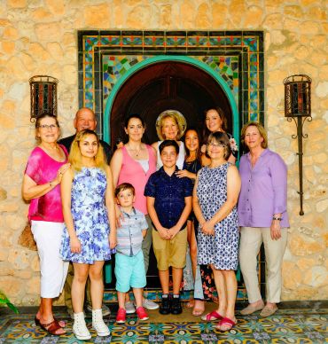 A multi-generational family posing in front of a decorative stone wall and arched doorway.