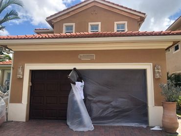 Person painting a garage door with dark paint in a residential area.