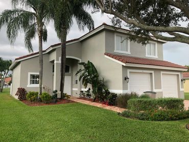 Modern two-story house with a well-maintained lawn and palm trees.