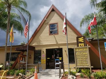 A rustic A-frame building with flags and a welcome sign in front.