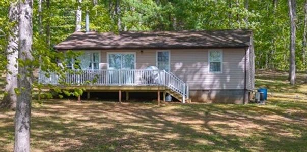 Small house with a wooden deck surrounded by trees in a forested area.