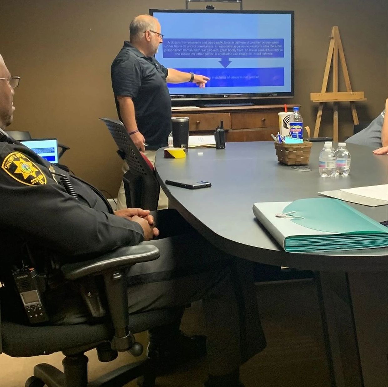 A man presenting information on a screen to a group in a meeting room.