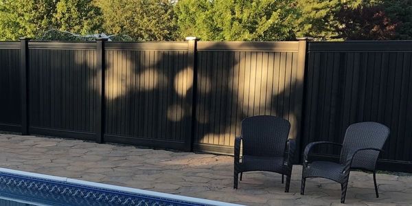 Two black chairs by a poolside with a dark fence and trees in the background.