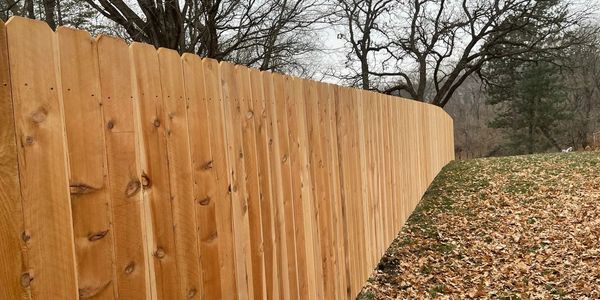 New wooden fence along a wooded area with fallen autumn leaves.