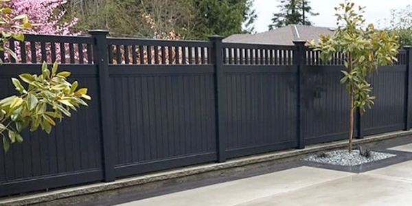 Modern black vinyl privacy fence with decorative top panels in a backyard.